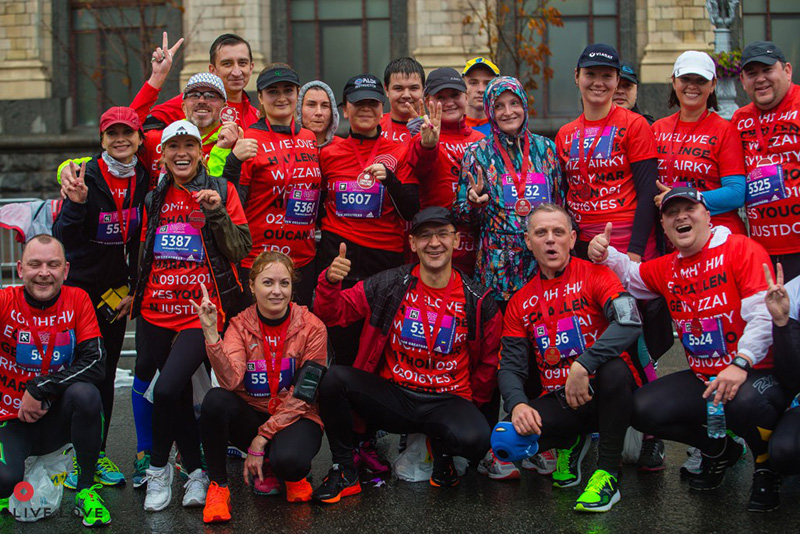Велика група щасливих бігунів команди LIVE.LOVE Run у червоних футболках позує для фото після Київського марафону