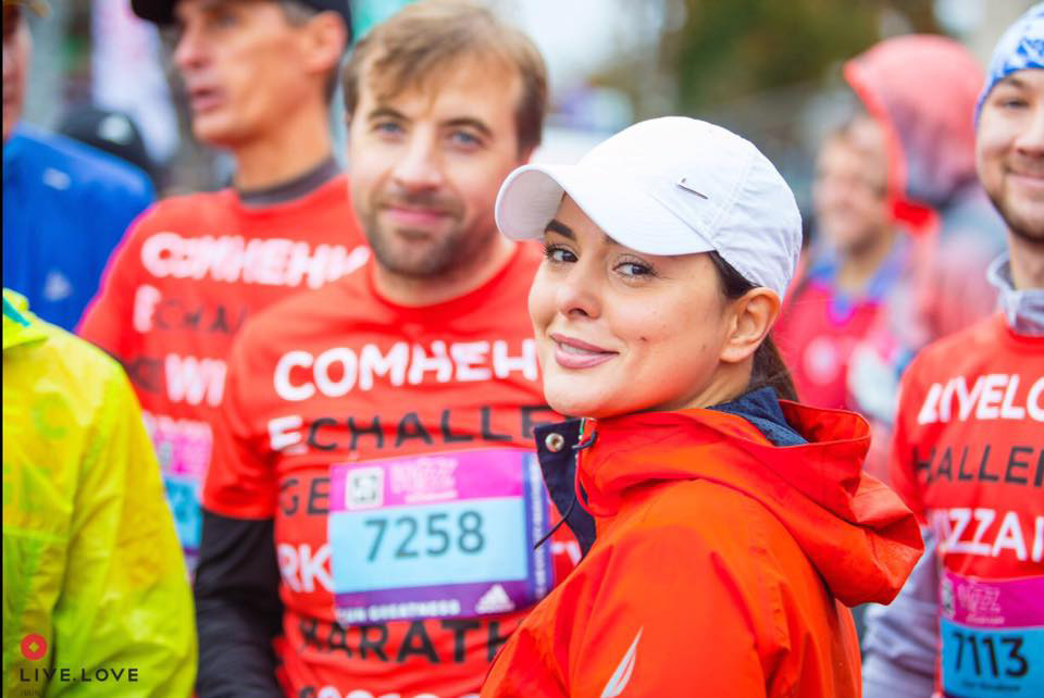 Усміхнена учасниця команди LIVE.LOVE Run у білій кепці та помаранчевій куртці на Київському марафоні